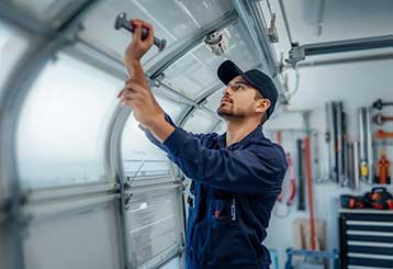 Technician in navy uniform repairing a residential garage door interior with professional tools in Antelope CA.
