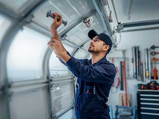 Technician in navy uniform repairing a residential garage door interior with professional tools in Antelope CA.