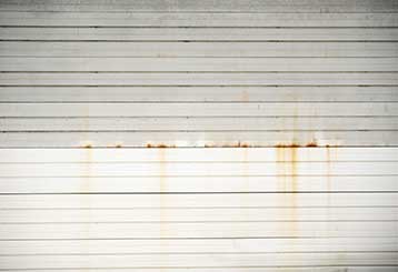 White garage door with rusty stains and horizontal paneling before cleaning.