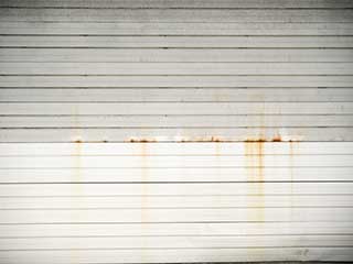 White garage door with rusty stains and horizontal paneling before cleaning.