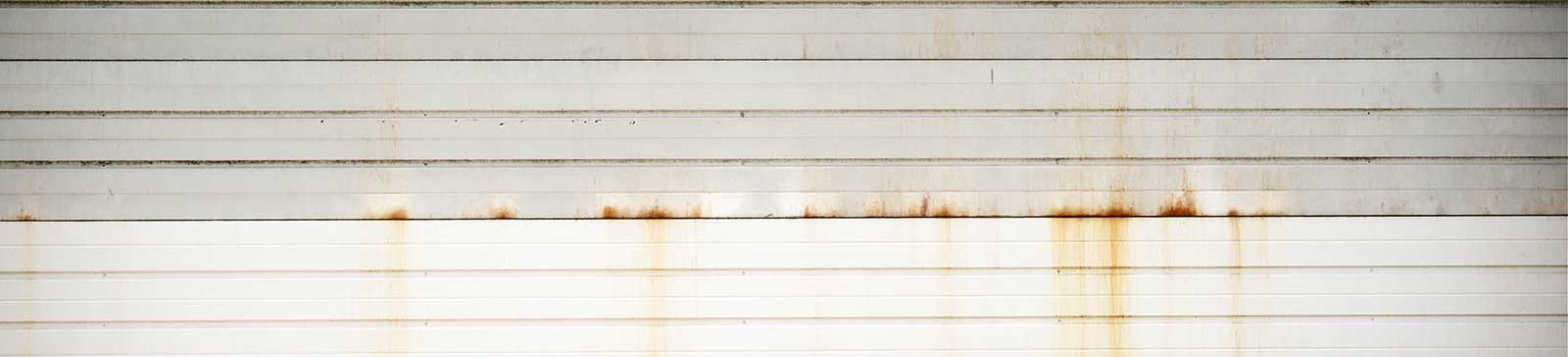 White garage door with rusty stains and horizontal paneling before cleaning.